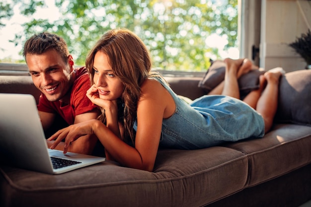 Jeune couple à l'aide d'un ordinateur portable allongé sur le canapé