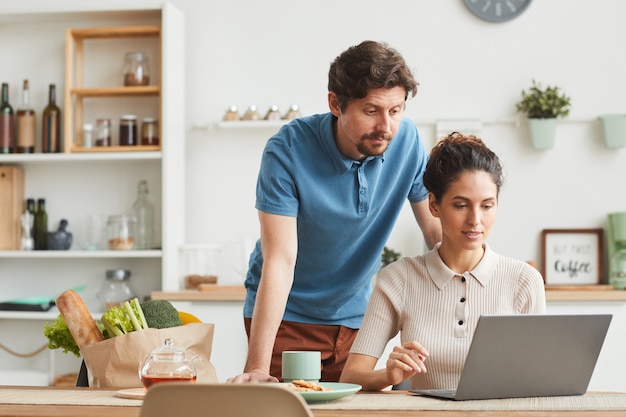 Jeune couple à l'aide d'un ordinateur portable à la maison, ils commandent des produits en ligne