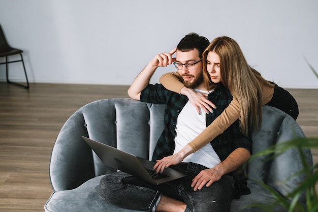 Jeune couple à l'aide d'un ordinateur portable et reposant sur le canapé à la maison ensemble.