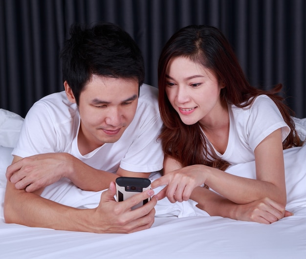 jeune couple à l&#39;aide de téléphone portable sur le lit dans la chambre à coucher