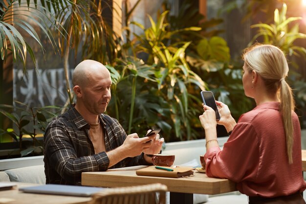 Jeune couple à l'aide de téléphones mobiles à la table lors de la réunion au café internet