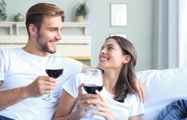 Jeune couple aimant boire un verre de vin rouge dans leur salon