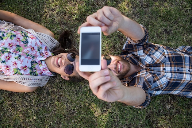 Jeune couple allongé sur l&#39;herbe prenant selfie
