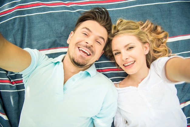 Jeune couple allongé sur la pelouse du parc et se selfie.