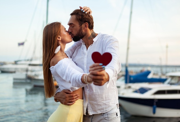 Un jeune couple d'amants s'embrassant tenant un cœur rouge montrant leur amour dans un club de yacht concept d'amour romantique