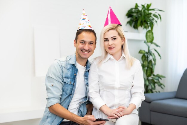 Jeune couple ou amis en chapeaux de fête s'amusant à une célébration virtuelle via un appel vidéo.