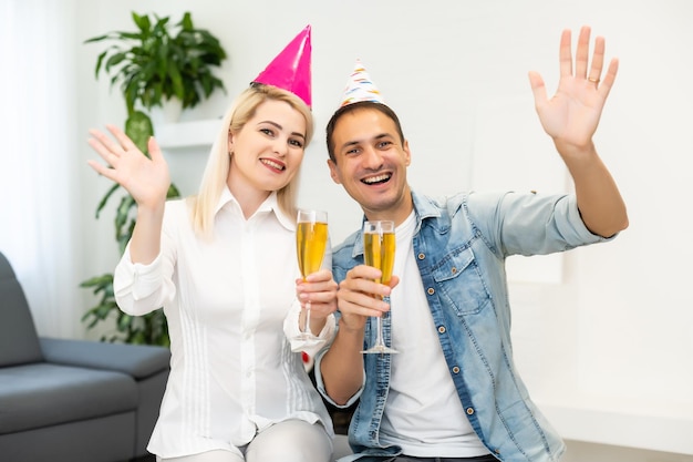 Jeune couple ou amis en chapeaux de fête s'amusant à une célébration virtuelle via un appel vidéo.