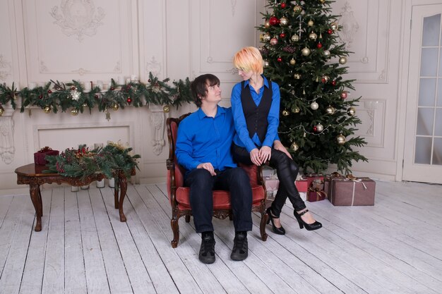 Jeune couple amoureux assis sur un canapé à la maison sur l'arbre de Noël en arrière-plan
