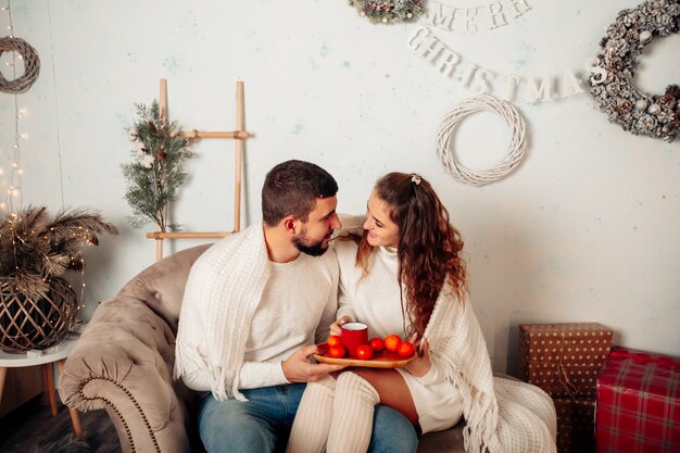 jeune couple amoureux assis sur un canapé et s'embrassant tout en tenant une tasse de thé dans un cadre de noël