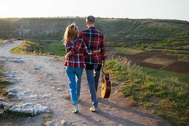 Jeune couple amoureux assis sur le parc pendant que ces jeunes jouent de la guitare au coucher du soleil.