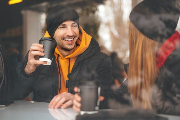 Jeune couple d'amoureux buvant du café dans un café derrière la vitre