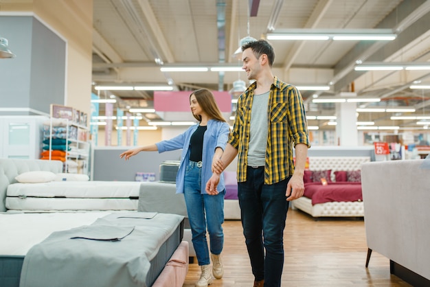 Jeune couple amoureux choisissant lit dans un magasin de meubles.