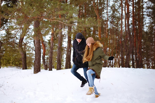 Jeune couple amoureux courir et se tenir la main dans la forêt d'hiver enneigée