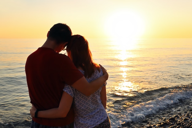 Jeune couple amoureux dans une étreinte au coucher du soleil au bord de la mer