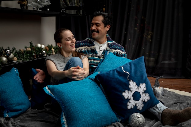 Jeune couple amoureux embrassé dans leur salon une nuit de Noël allongé avec des oreillers.