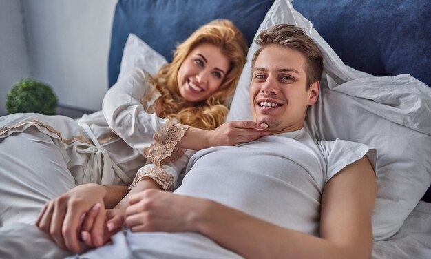 Un jeune couple amoureux est allongé dans son lit, souriant et s'amusant.