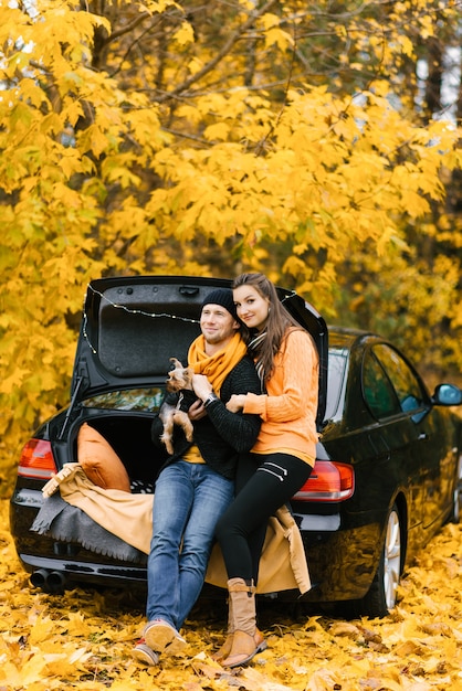 Un jeune couple amoureux est assis sur le coffre ouvert d'une voiture