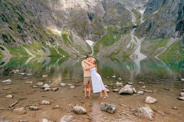 Jeune couple d'amoureux étreignant dans l'eau froide du lac entre les hautes montagnes en journée d'été.