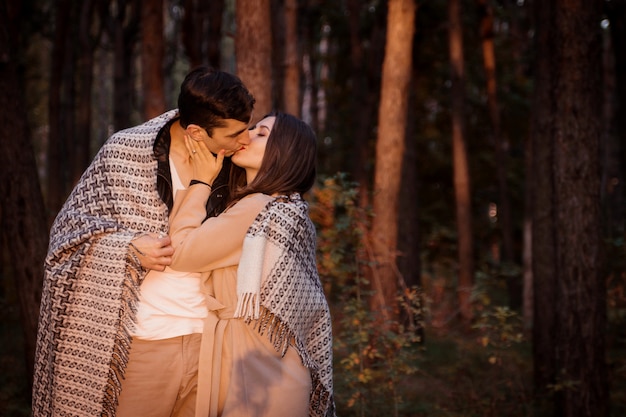 Jeune couple amoureux étreignant et s'embrasser recouvert de couverture dans la forêt d'automne. Heureux homme et femme ayant rendez-vous romantique