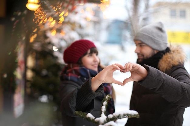 Jeune couple d'amoureux faisant coeur avec les mains à l'extérieur le jour de l'hiver