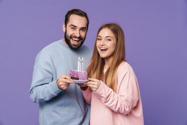 un jeune couple d'amoureux heureux et émotionnel isolé sur un mur violet avec un gâteau d'anniversaire.