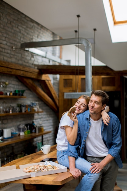 Jeune couple amoureux mangeant une pizza dans la maison rustique