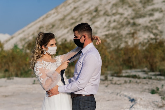 Jeune couple amoureux marchant dans des masques médicaux dans le parc le jour de leur mariage.