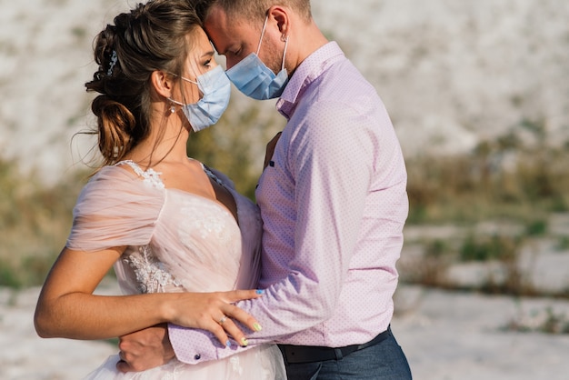 Jeune couple amoureux marchant dans des masques médicaux dans le parc pendant la quarantaine le jour de leur mariage.