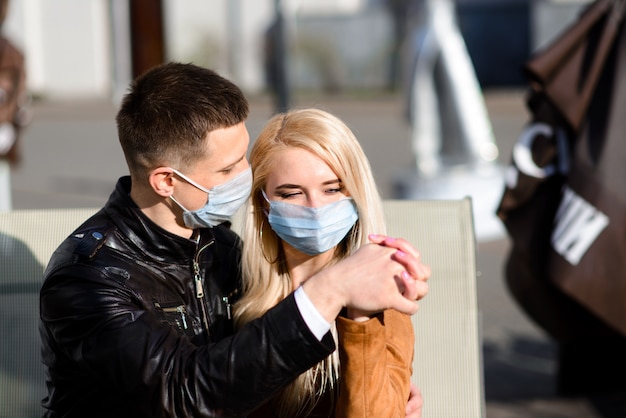 Jeune couple amoureux en masque médical de protection sur le visage en plein air dans la rue.