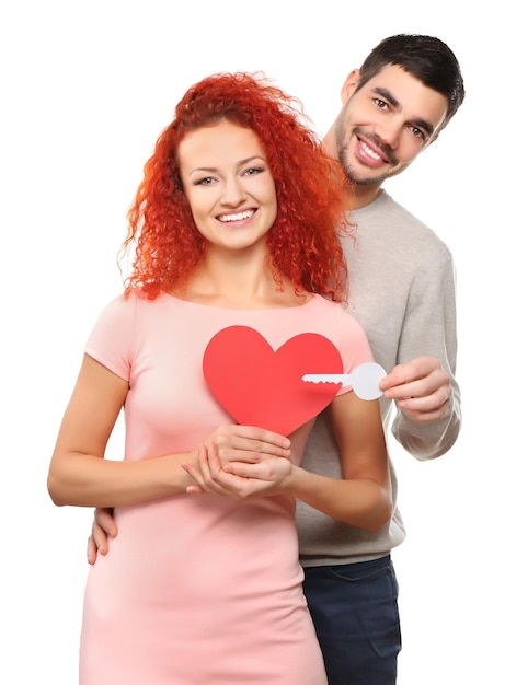 Jeune couple amoureux tenant coeur rouge papier et clé isolé sur blanc