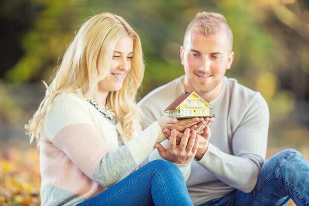 Jeune couple d'amoureux tenant une petite maison modèle.