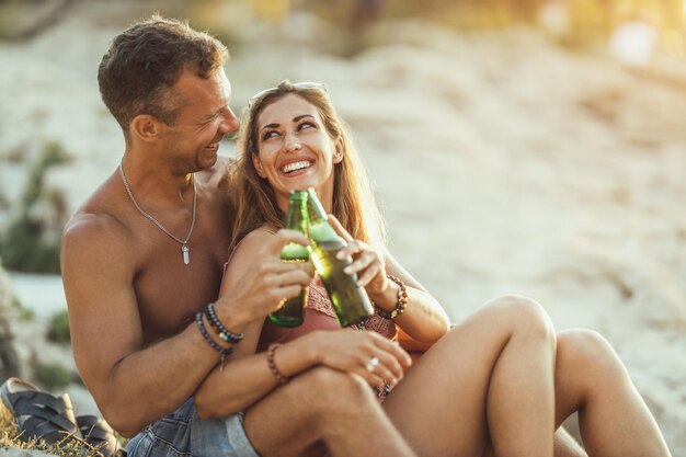 Jeune couple appréciant leur amour et buvant de la bière sur la plage au bord de la mer.
