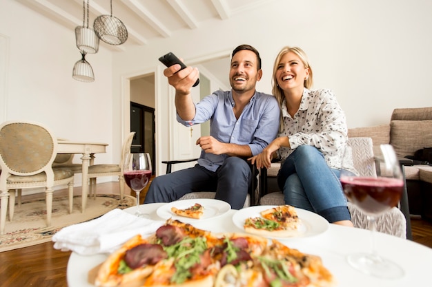 Jeune couple appréciant manger des pizzas et regarder la télévision à la maison