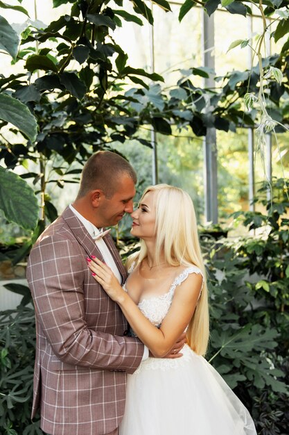 Jeune couple appréciant des moments romantiques en marchant dans le parc. Élégante mariée et le marié posant et s'embrassant dans le parc le jour de leur mariage. Mariée élégante dans une belle robe blanche, marié en costume.