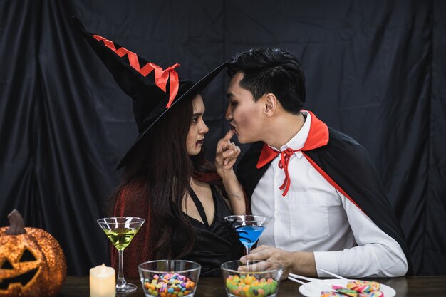 Jeune couple asiatique en costume de sorcière et dracula avec célébrer la fête d'Halloween pour un verre à trinquer et boire au festival d'Halloween. Un couple en costume célèbre le fond de tissu noir de la fête d'Halloween.