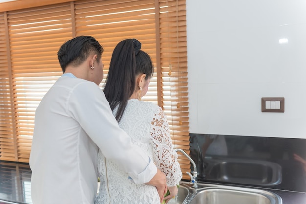 Jeune couple asiatique cuisine avec loveshe coupe des légumes qu'il embrasse de dos