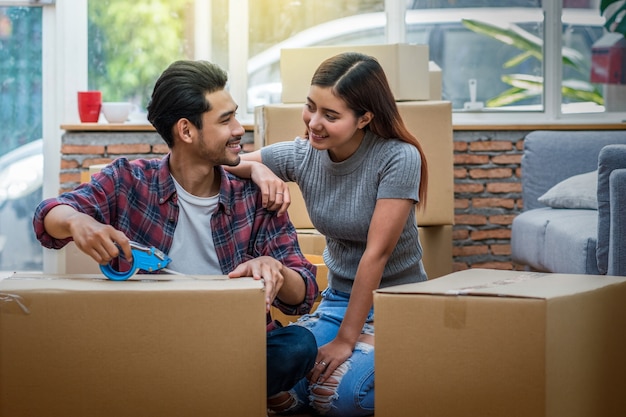 Jeune couple asiatique, emballant la grande boîte en carton pour emménager dans la nouvelle maison