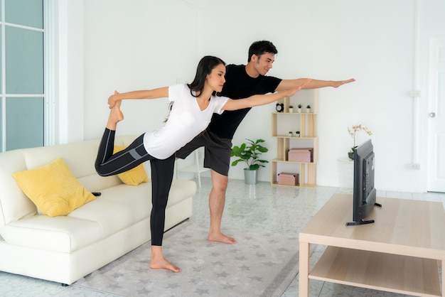 Jeune couple asiatique, faire du yoga ensemble et regarder la télévision à la maison