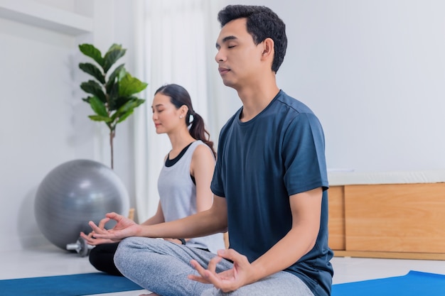 Jeune couple asiatique fait de l'exercice et joue au yoga ensemble à la maison