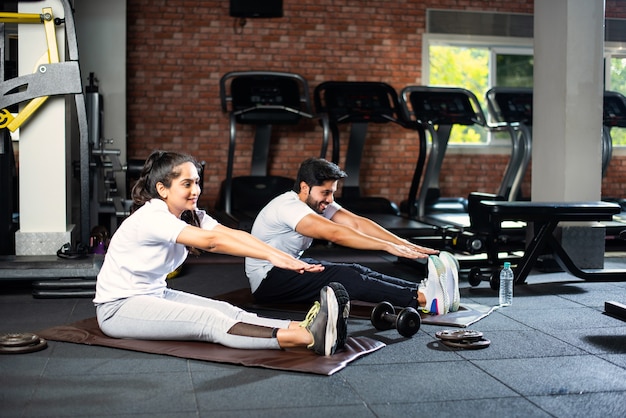 Jeune couple asiatique indien sportif s'étirant dans la salle de gym après l'exercice pour se rafraîchir, améliorer la flexibilité