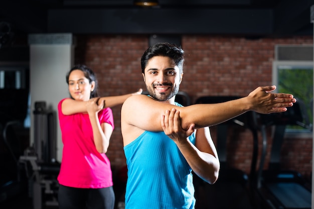 Jeune couple asiatique indien sportif s'étirant dans la salle de gym après l'exercice pour se rafraîchir, améliorer la flexibilité