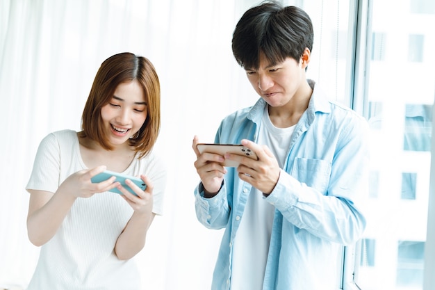 Jeune couple asiatique jouant à des jeux ensemble sur téléphones mobiles