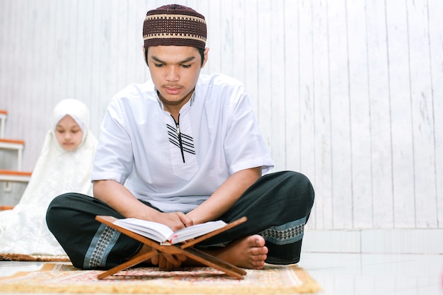 Jeune couple asiatique mulim assis et lisant le livre saint AlQuran ensemble sur le tapis de prière à la maison