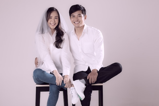 Jeune couple asiatique séduisant portant une chemise blanche et un jean femme portant un voile de mariage assis ensemble en souriant. Concept pour la photographie avant le mariage.
