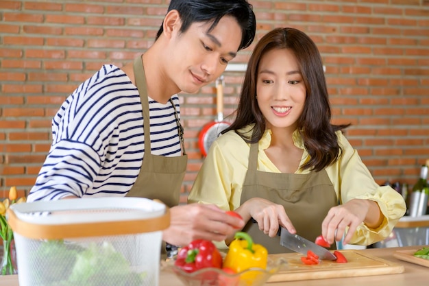 Jeune couple asiatique souriant portant un tablier dans le concept de cuisine de la salle de cuisine