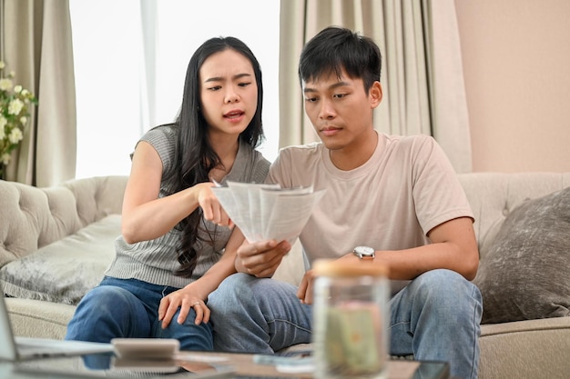 Un jeune couple asiatique stressé planifie ses économies et gère ensemble ses factures domestiques.