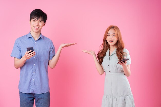 Jeune couple asiatique utilisant un smartphone sur fond rose