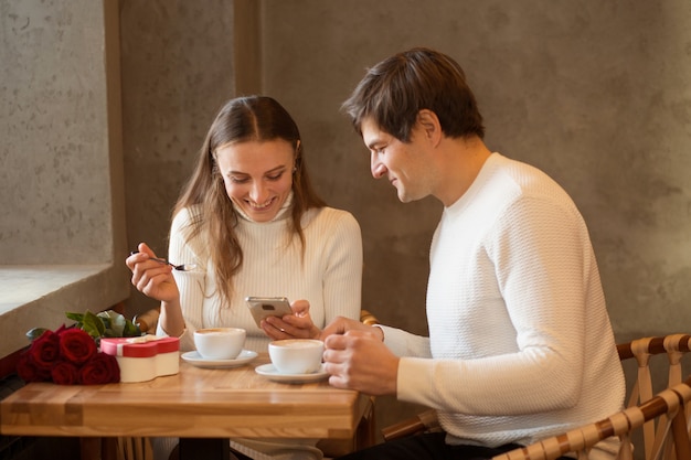 Jeune couple assis au café. Shopping en ligne. Bouquet de roses et cadeau