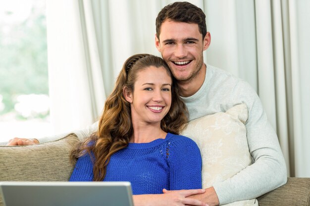 Jeune couple assis sur un canapé et utilisant un ordinateur portable dans le salon