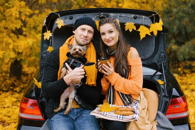 Jeune couple assis sur le coffre d'une voiture